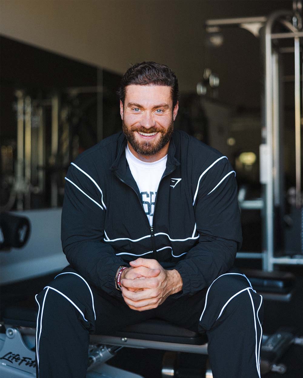 Man sitting in a gym front on wearing blue athleisure. Sporting for a men's gym do.